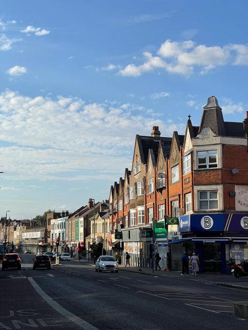 The image shows a quiet residential street lined with Victorian-style terraced houses, predominantly white with some featuring brickwork exteriors and bay windows. The street is partly paved with conc